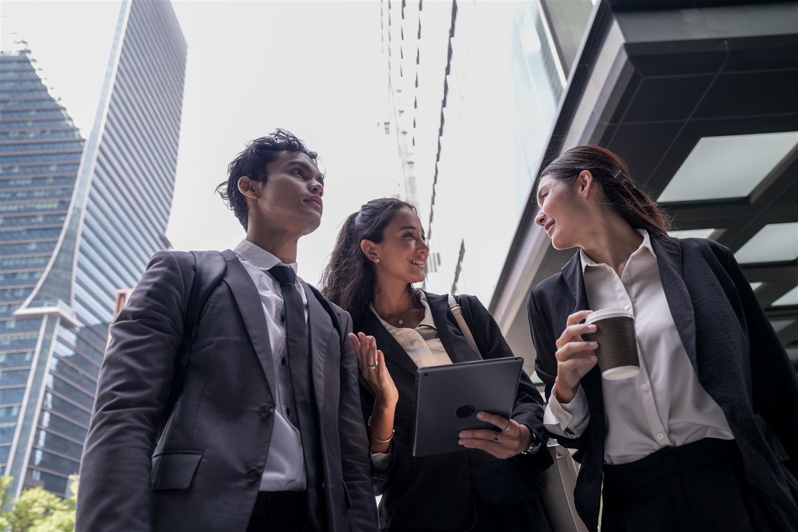 Malaysian facility managers with a tablet discussing preventive maintenance software outside a city office tower. Nexus ICMMS planned preventive maintenance (PPM) schedules, work orders and completion proof for multi-site operations